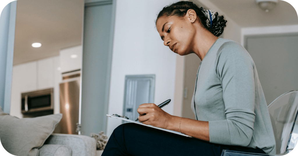 A woman sits at a table writing on a clipboard, capturing the careful planning and documentation involved in employee offboarding.